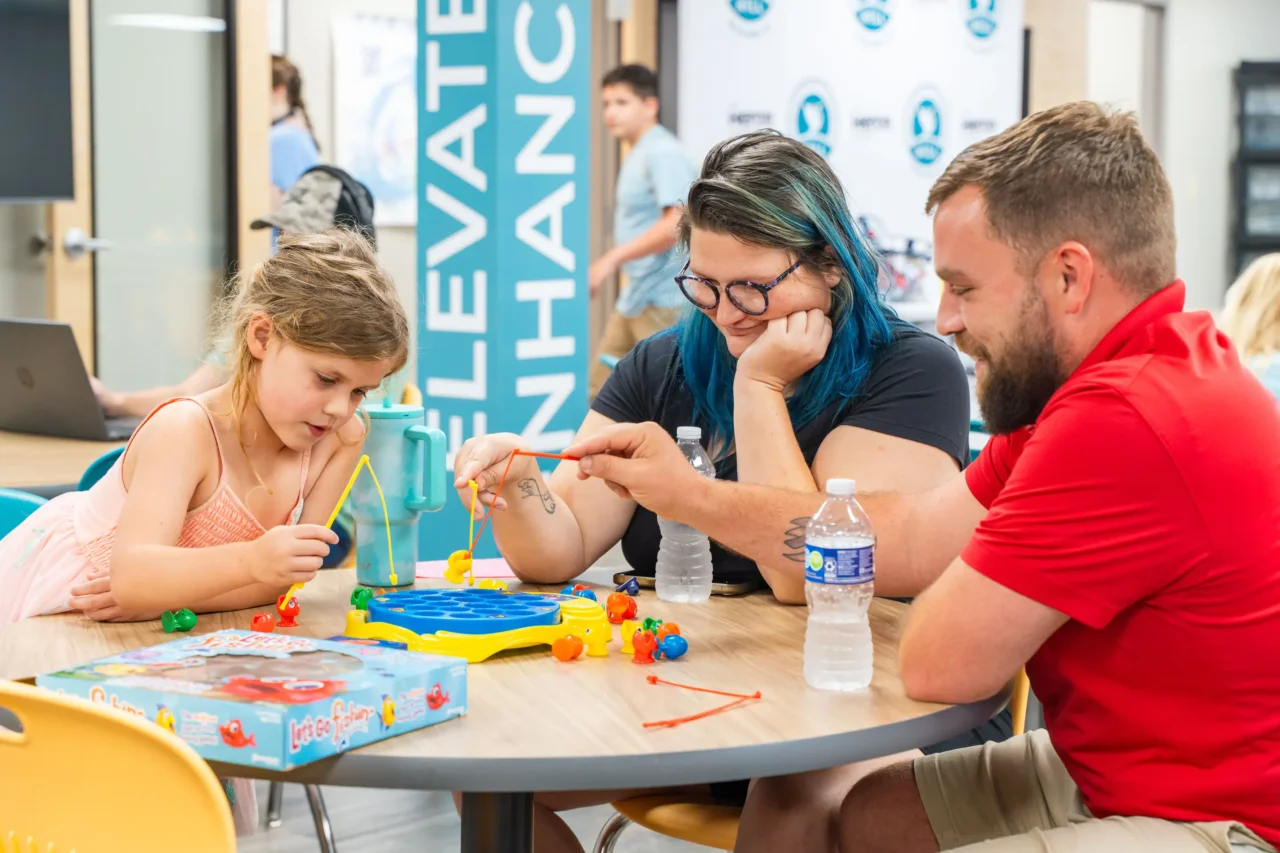Adults and child engage in a fishing game at a community event, emphasizing learning and togetherness.