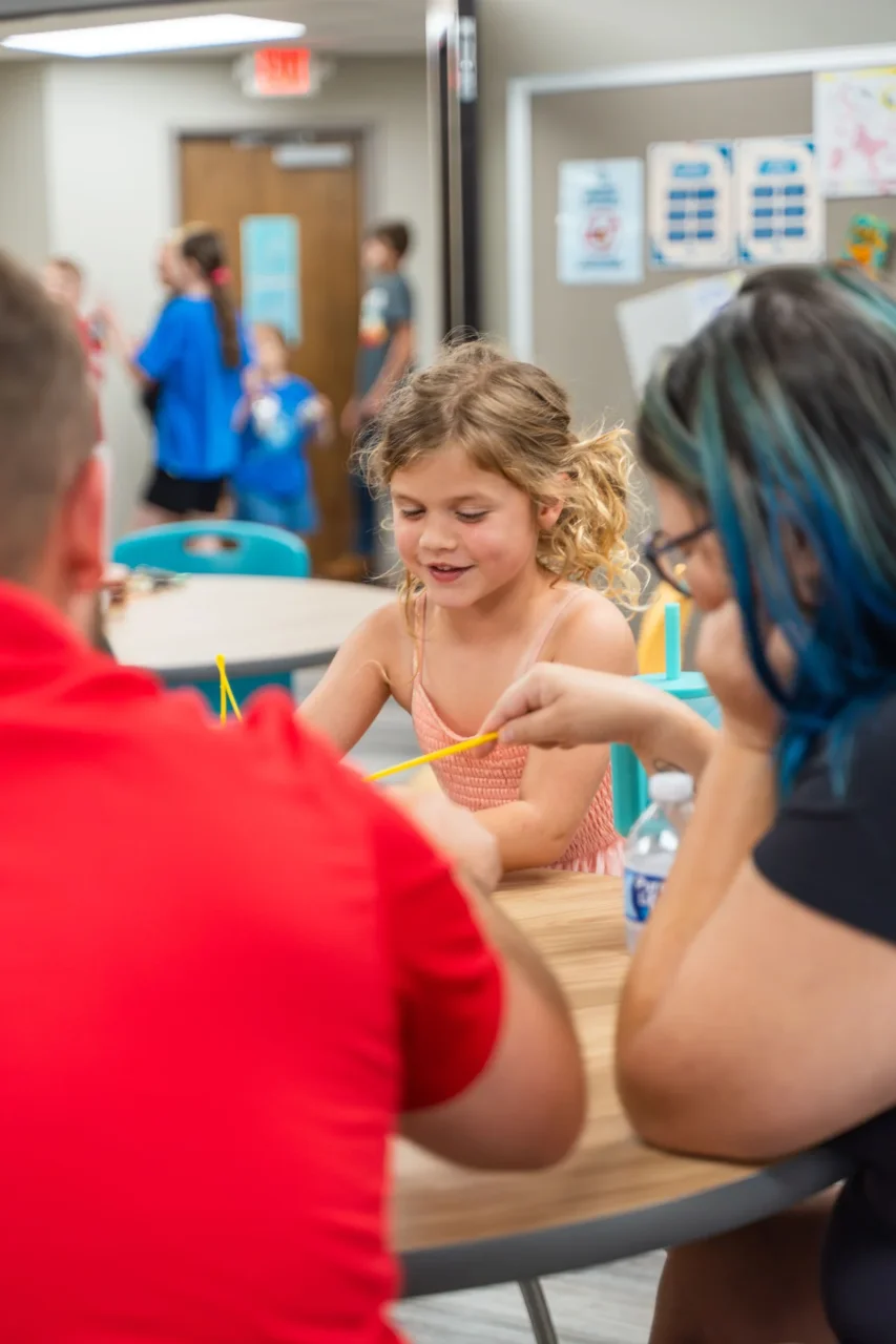 Young girl engaging in a creative activity with adults in a vibrant school community setting.