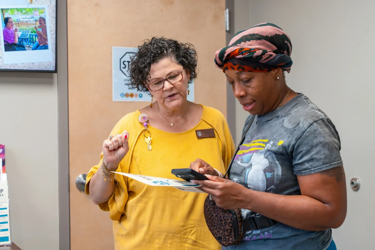 Two women at Cyber Academy discussing a document and phone, highlighting in-person support and connection.