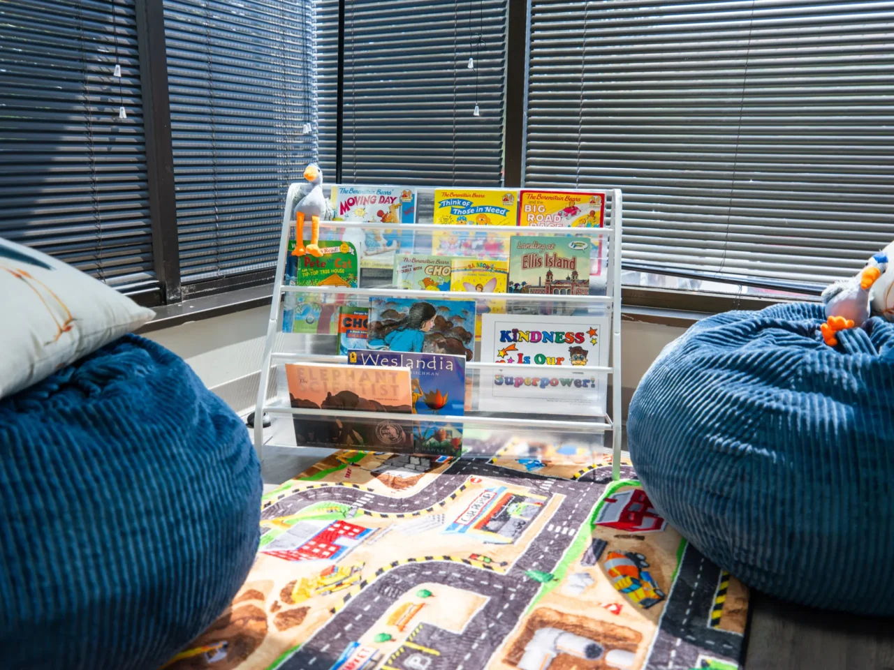 Children's reading area with blue bean bags and book rack featuring titles like "Ellis Island" and "Kindness Is Our Superpower.