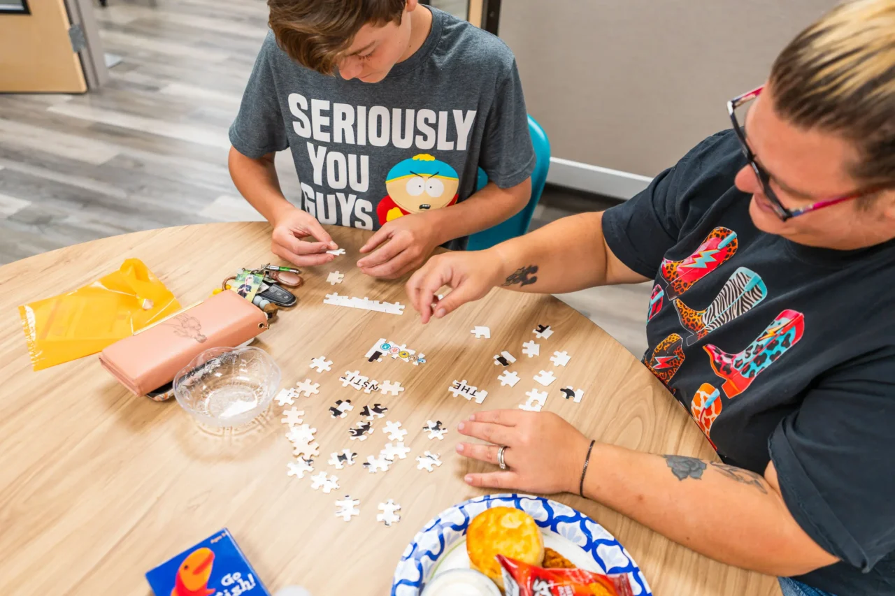 Two people assembling a puzzle at a community event, accompanied by snacks on the table.