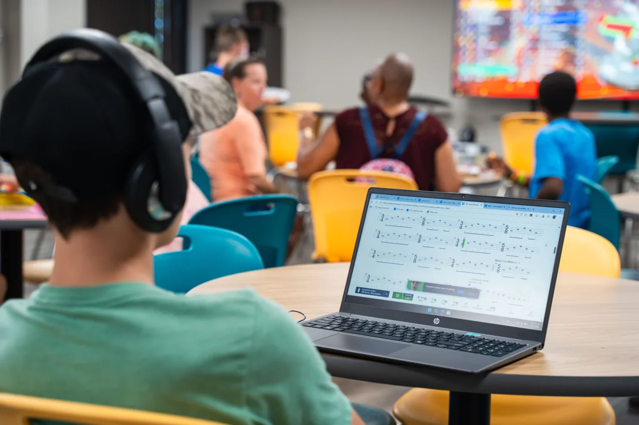 Student wearing headphones using a laptop in a Heron Virtual Academy learning lab, surrounded by peers.