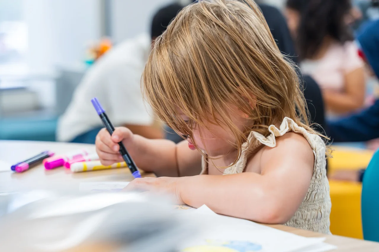 Child engaged in drawing with markers, highlighting creative learning in a supportive cyber academy environment.