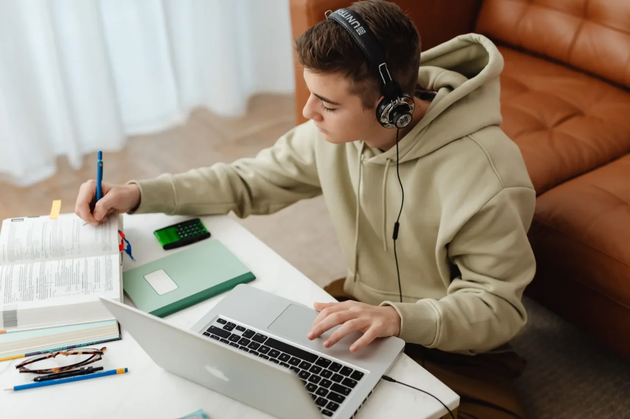 Student in headphones studying with a laptop and textbook, representing Heron Virtual Academy's in-person support.