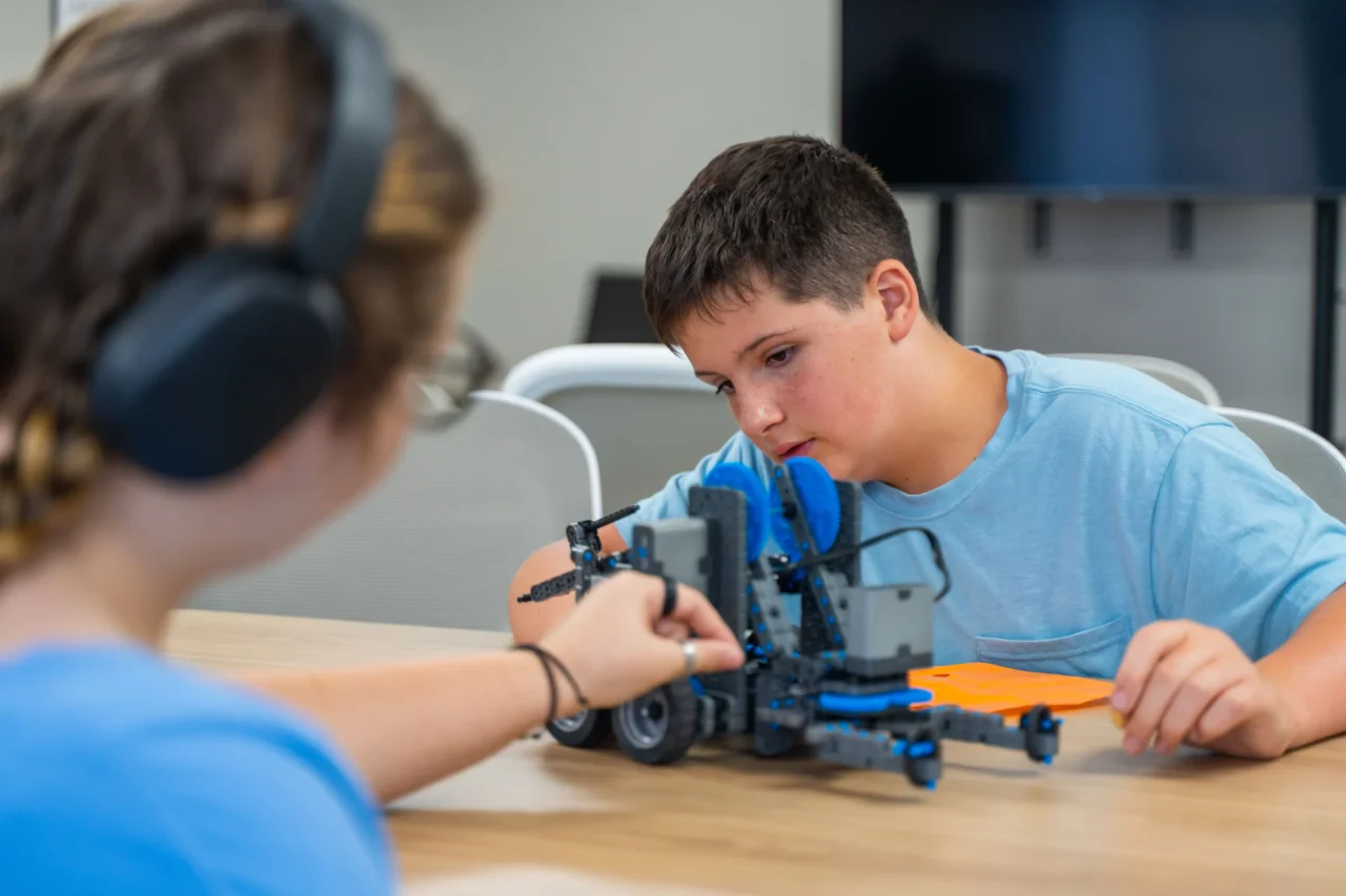 Students engage with a robotics project in a shared learning space, highlighting age-dedicated classrooms.