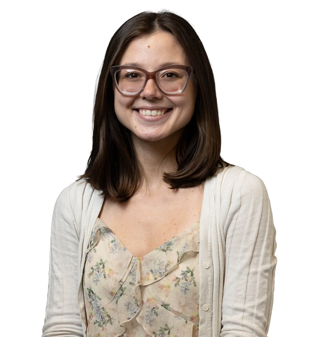 Smiling woman with dark hair and glasses wearing a floral blouse and cardigan, representing one community.